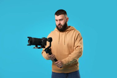 Açık mavi arkaplanda kameralı titreşim dengeleyici kullanan kameraman