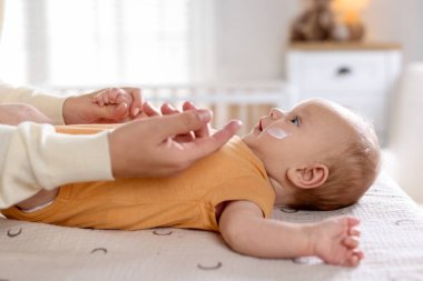 Anne evde masasını değiştirirken bebeğinin yüzüne krem sürüyor.