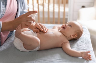 Anne, bebeğin cildine krem sürüyor. Evde masaları değiştiriyor. Yakın plan.