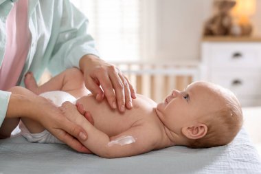 Anne bebeğinin koluna krem sürüyor evde masasını değiştiriyor, yakın plan.