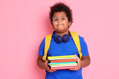 Kulaklıkları, not defterleri ve pembe arka planı olan sevimli küçük bir çocuk.