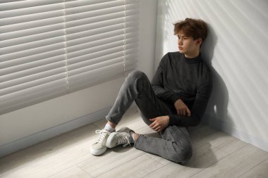 Evdeki pencerenin yanında depresyonda olan genç bir çocuk.