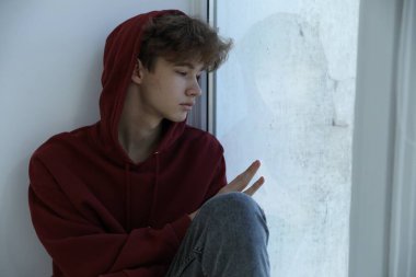 Depresyondaki genç çocuk pencerenin yanında, mesaj için yer var.