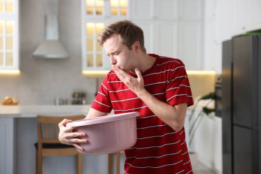 Kapalı alanda mide bulantısı çeken genç bir adam.