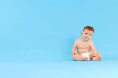 Açık mavi arka planda oturan şirin küçük bebek, mesaj için boşluk