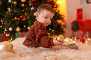 Noel için dekore edilmiş odada yerde oturan sevimli küçük bebek.