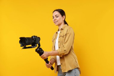 Sarı arka planda kamerası olan titreşim sabitleyici kullanan kameraman, düşük açılı görünüm