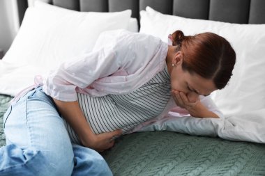 Evde yatağında mide bulantısı çeken hamile bir kadın.