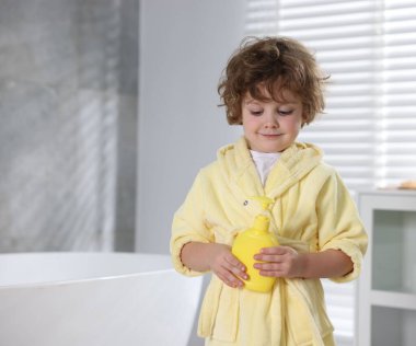 Banyoda bir şişe banyo ürünüyle sarı bornozlu şirin bir çocuk. Metin için boşluk