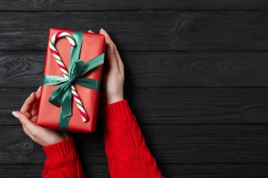 Elinde süslü Noel hediyesi olan siyah tahta arka planda şeker kamışı taşıyan bir kadın. Metin için boşluk