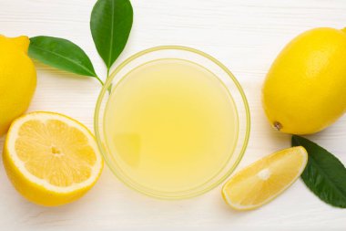 Bardakta limon suyu, yapraklar ve beyaz ahşap masada taze limonlar.