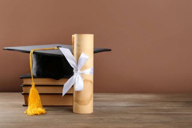 Mezuniyet şapkası, diploma ve kahverengi arka planla ahşap masadaki kitaplar. Metin için boşluk