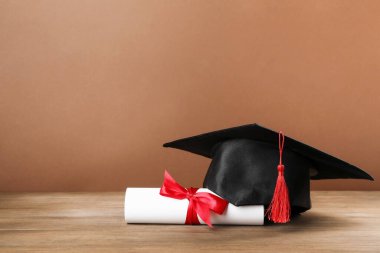 Mezuniyet şapkası ve diploması, kahverengi arka planla ahşap masada. Metin için boşluk
