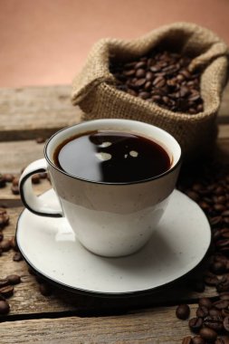 Kahverengi arka planda kahve fincanı ve ahşap masada fasulye, yakın plan.