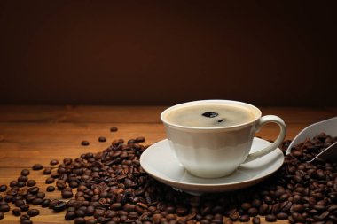 Kahverengi arka planda kahve fincanı ve ahşap masada fasulye, yakın plan. Metin için boşluk