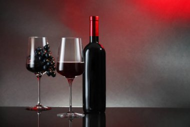 Kırmızı şarap bardakta, şarap şişesi ve üzüm siyah masada renk arka planına karşı. Metin için boşluk