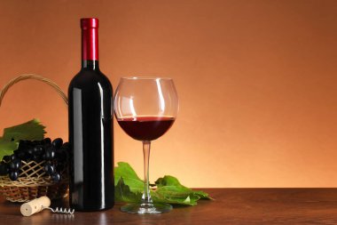 Bardakta kırmızı şarap, şişe, tirbuşon ve üzümler ahşap masada kahverengi arka planda, mesaj için boşluk