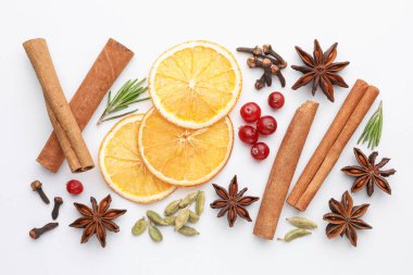 Farklı baharatlar, kızılcıklar, kuru portakal dilimleri ve beyaz masada taze biberiye, düz uzanmış.