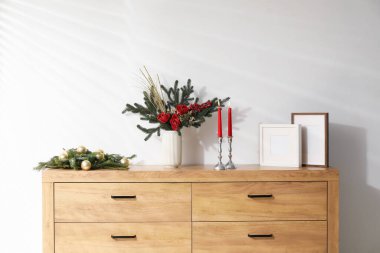 Beyaz duvarın yanındaki ahşap dolapta farklı bir Noel dekoru var.