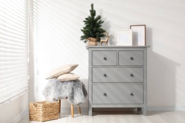 Beyaz duvarın yanındaki gri dolapta farklı Noel dekorları ve çerçeveler var.