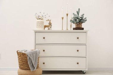 Beyaz duvarın yanındaki dolapta Noel süsleri ve yanan mumlar.