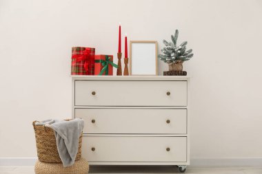 Beyaz duvarın yanındaki dolapta Noel dekorasyonu, çerçeve ve yanan mumlar.