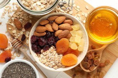 Tahıl yapıyorum. Yulaf gevreği, kurutulmuş meyve ve diğer malzemeler beyaz masada, düz yerde.