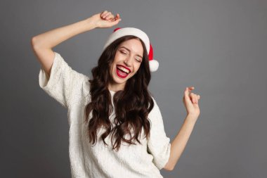 Noel Baba şapkalı güzel kadın gri arka planda eğleniyor. Noel partisi