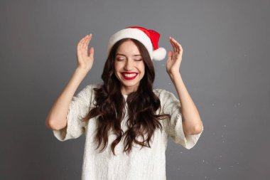 Noel Baba şapkalı güzel kadın gri arka planda eğleniyor. Noel partisi