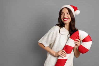 Gri arka planda Noel Baba şapkalı ve baston şekerli yastıklı güzel bir kadın. Mesaj için yer var. Noel sezonu