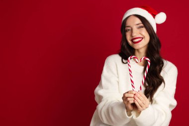 Kırmızı arka planda Noel Baba şapkası ve şeker kamışı olan güzel bir kadın. Mesaj için yer var. Noel sezonu
