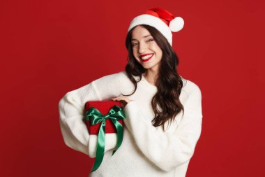 Kırmızı arka planda Noel Baba şapkası ve Noel hediyesi olan güzel bir kadın.
