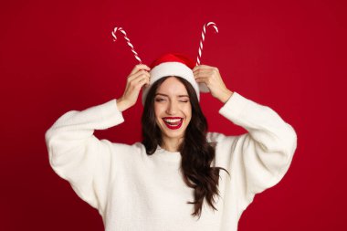 Kırmızı arka planda Noel Baba şapkası ve şeker kamışı olan güzel bir kadın. Noel sezonu