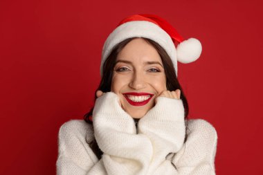 Kırmızı arka planda Noel Baba şapkalı güzel bir kadın. Noel sezonu