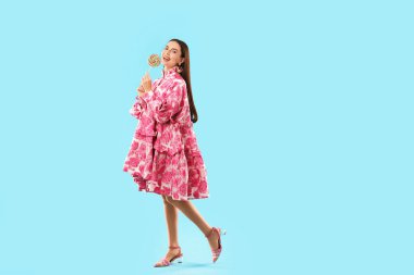 Açık mavi arka planda lolipopu olan güzel bir kadın.