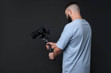 Kameraman siyah arkaplanlı, titreşimli dengeleyici kullanıyor. Metin için boşluk