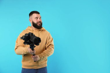 Kameraman açık mavi arkaplanda kameralı titreşimli dengeleyici kullanıyor. Metin için boşluk