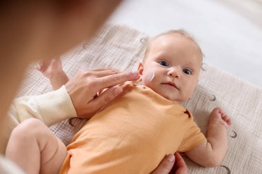 Anne evde masasını değiştirirken bebeğinin yüzüne krem sürüyor.