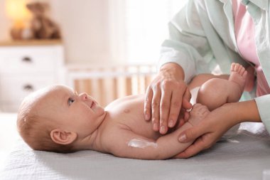 Anne bebeğinin koluna krem sürüyor evde masasını değiştiriyor, yakın plan.