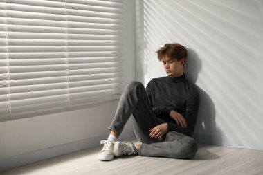 Evdeki pencerenin yanında depresyonda olan genç bir çocuk.