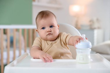 Evinde şezlongda yemek şişesi olan sevimli bir bebek.