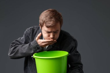 Gri arka planda bulantı çeken kovalı genç bir adam.