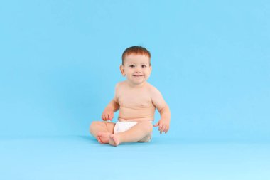 Açık mavi arka planda oturan şirin bir bebek.