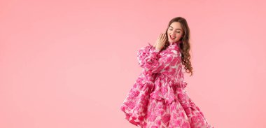 Pembe arka planda poz veren güzel giyimli genç bir kadın.