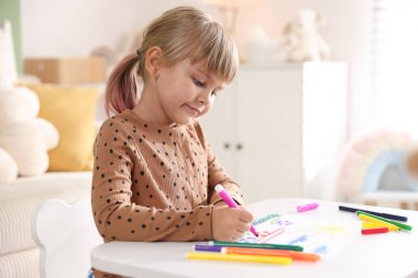 Beyaz masa içinde keçeli kalemle çizen sevimli küçük kız.