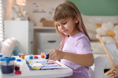 Beyaz masa içinde fırça çizen küçük kız.