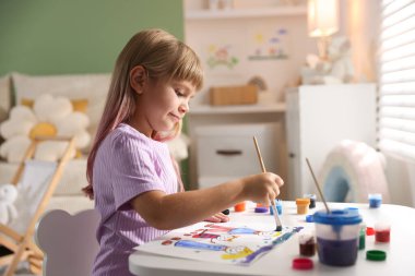 Beyaz masa içinde fırça çizen küçük kız.