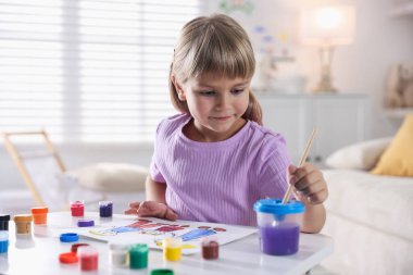 Beyaz masa içinde fırça çizen küçük kız.