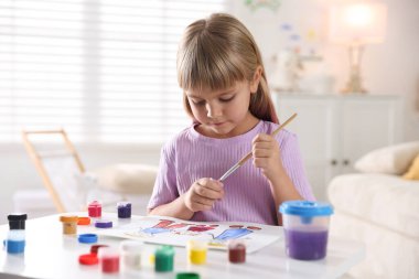 Beyaz masa içinde fırça çizen küçük kız.