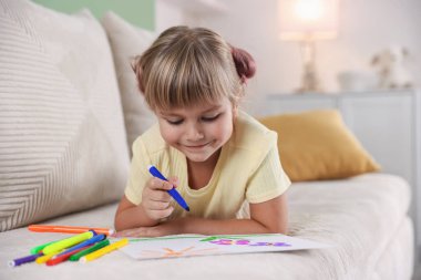 Evdeki kanepede keçeli kalemle çizen sevimli küçük kız.